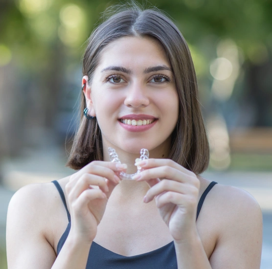Woman holding clear aligners in front of her teeth