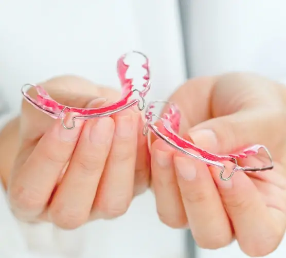 Patient's hands holding pink and white clear dental retainers.