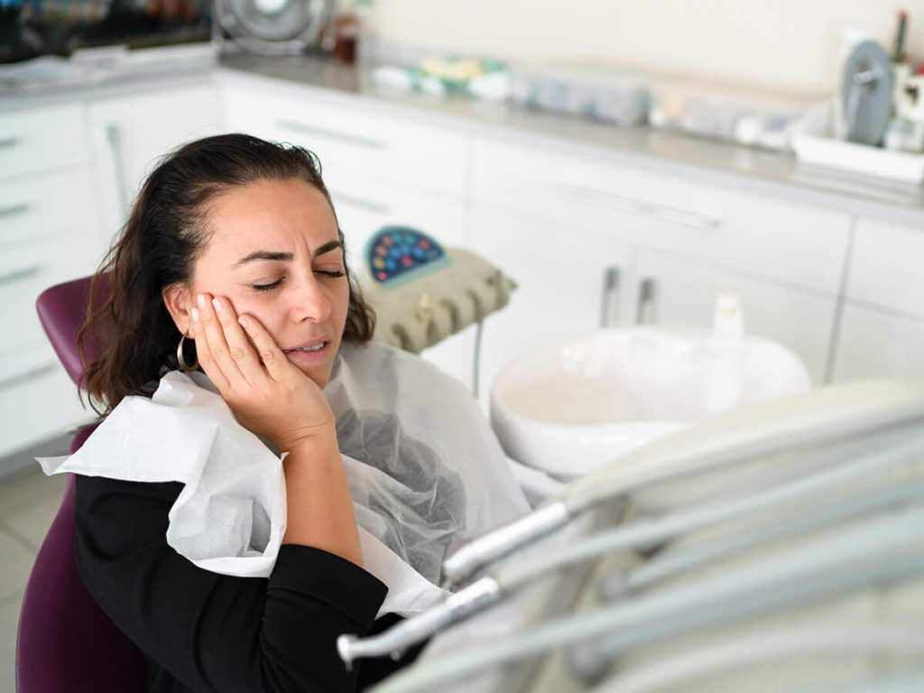 women in dental chair holding her jaw in pain