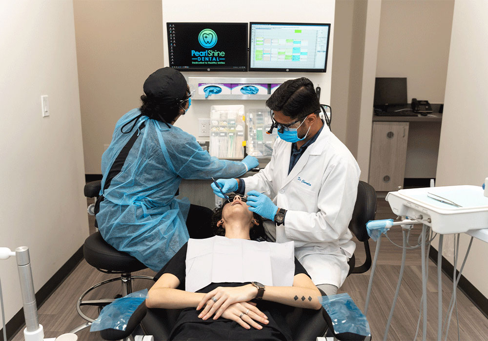 Dr. Charolia checking patient's teeth while an assistant checks charts on the screen behind them